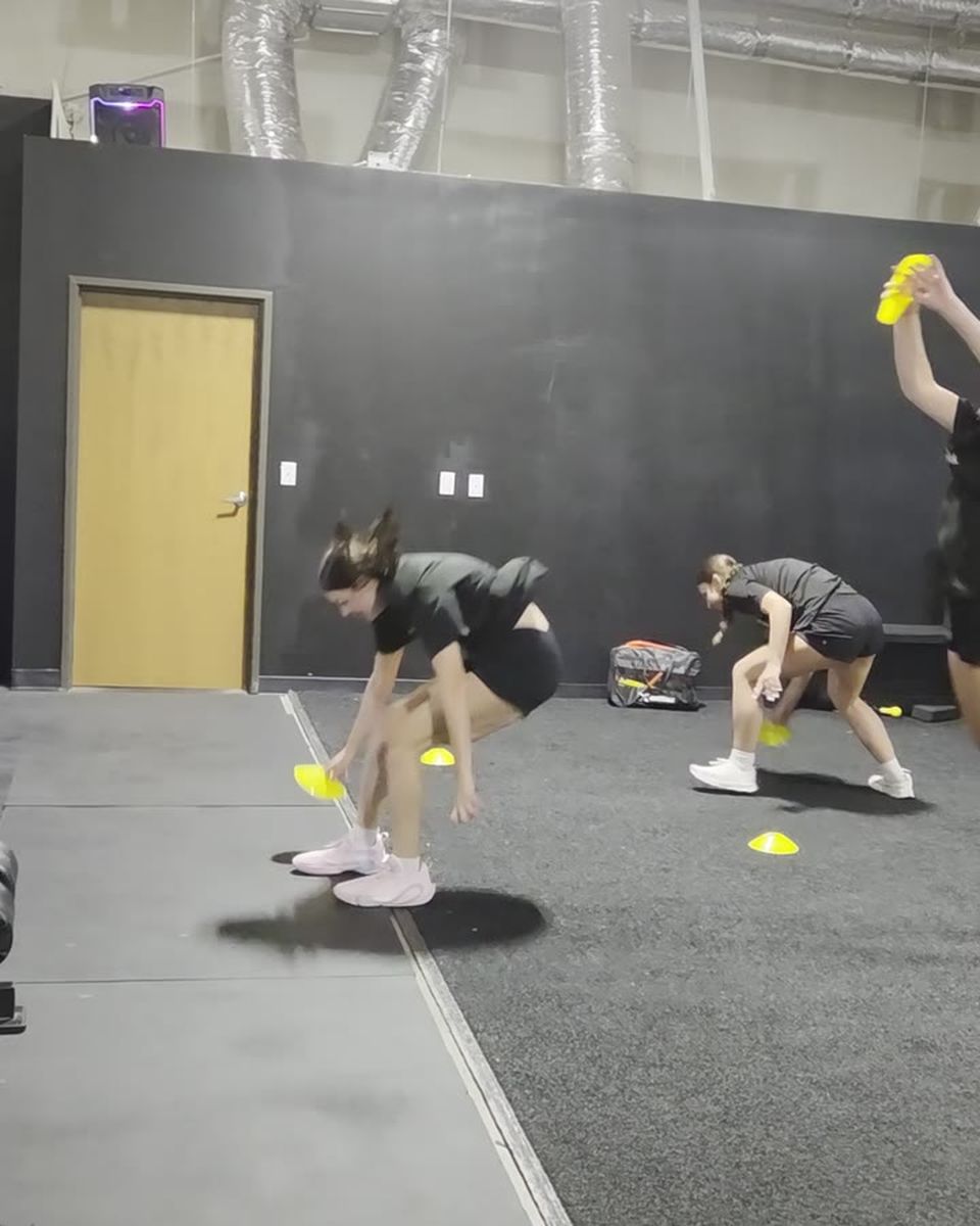 A group of young athletes racing each other to gather cones from the gym floor, bending to grab them and sprinting between them.