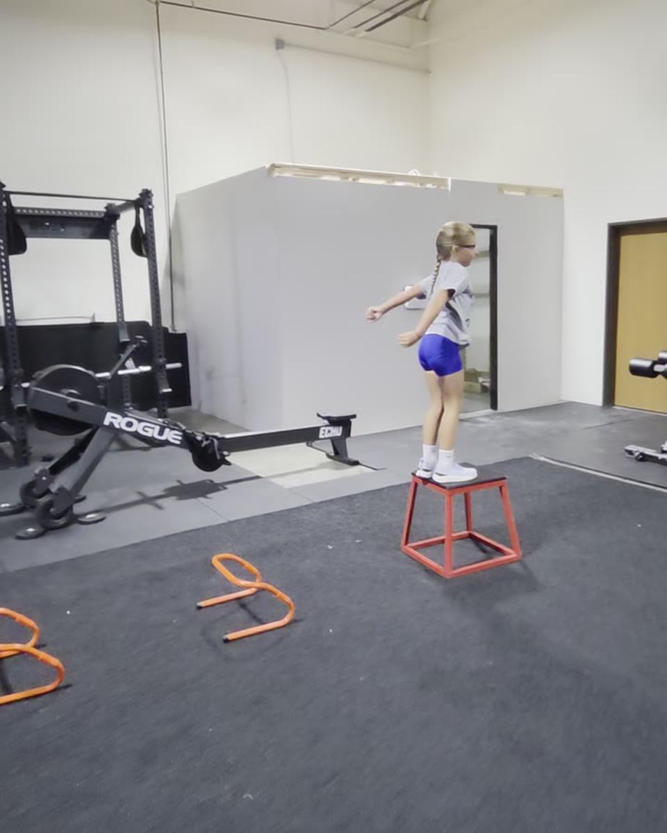 A young athlete balanced on a plyo box after jumping a line of hurdles.