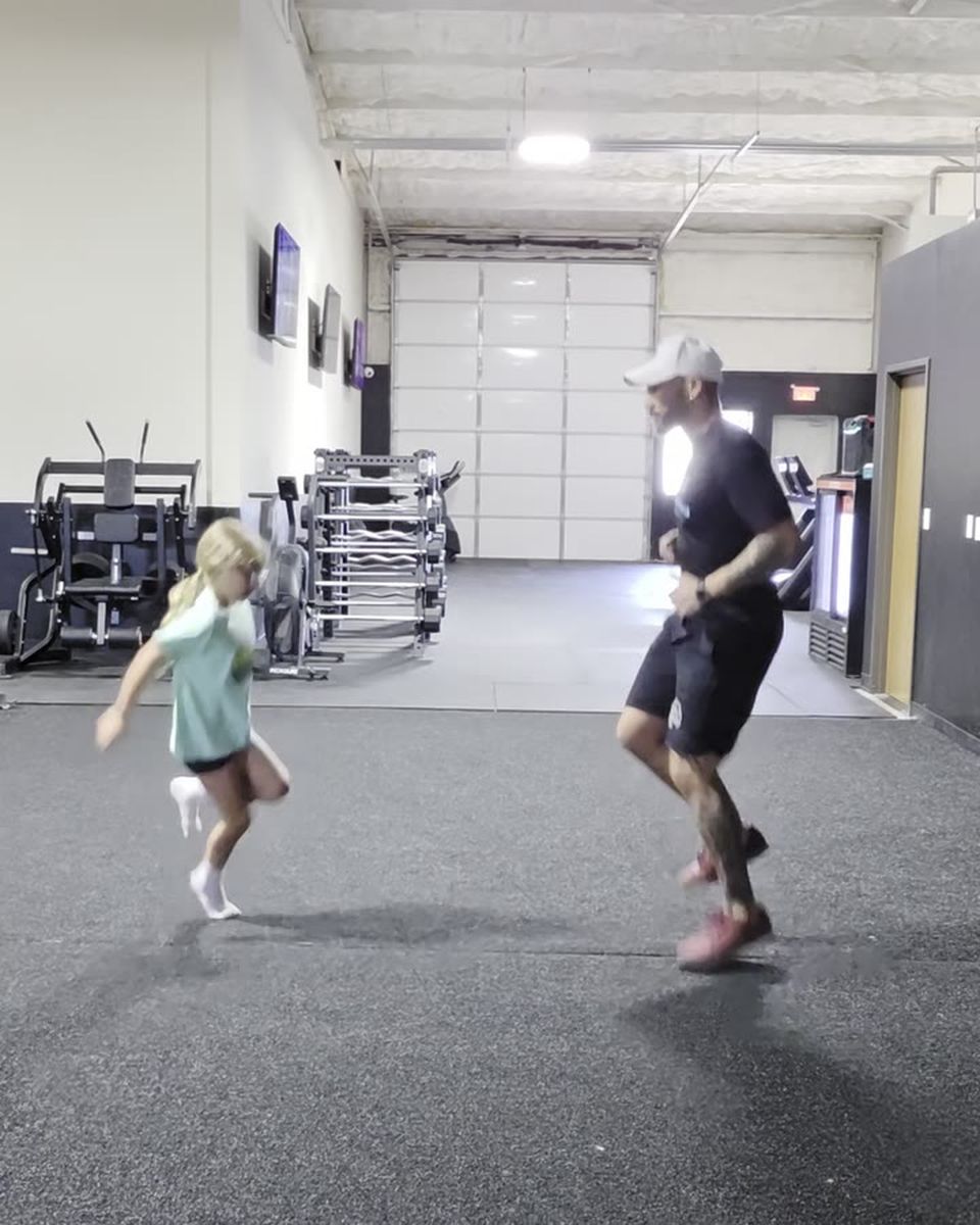 A coach working through sprint mechanics alongside a young athlete, both driving one knee up.