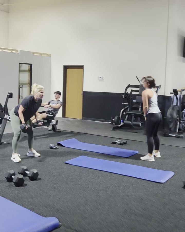 A woman rowing a dumbbell in a hinged position while other clients work through their own movements behind her.