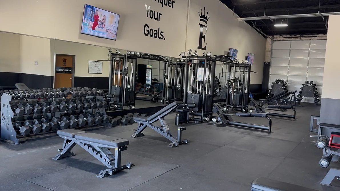 The training floor inside Empire Fitness in Glenpool: racks of dumbbells, adjustable benches, cable machines and open matted floor.